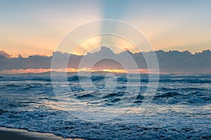 Spectacular sunrise seascape of ocean waves and sun beaming through the clouds