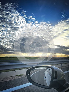 a spectacular sunrise seen from the window of a moving car, in the foreground the driving rearview mirror with the reflection of