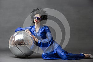 Spectacular Woman in a sparkly flared suit and afro wig poses with a disco ball