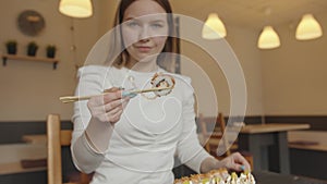 A spectacular young girl sits in a cafe and takes sushi maki from a plate and demonstrates it to the camera. Slow motion