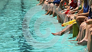 Spectators legs and feet as they sit on the edge of a clear clean swimming pool