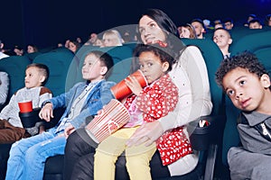 Spectators sitting in movie theatre and enjoying film, eating snacks.