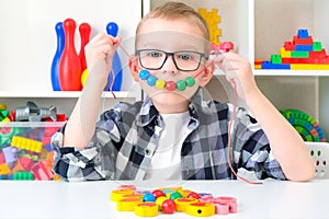 Speech therapy, the development of fine motor skills. Toddler boy is stringing beads on a string