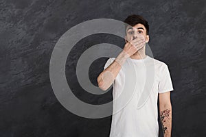 Speechless man covering mouth at gray studio background