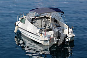 Speed boat with outboard boat motor and dark blue sunroof anchored in local harbor surrounded with calm clear blue sea