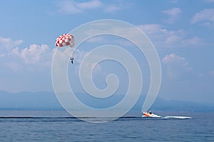 Speed boat pulling parachute with tourist on panoramic view of local bay over calm sea with mountains and cloudy blue sky in