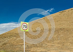 Speed limit sign with traffic in the background of blue sky and the yellow hillside