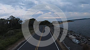 Speed ramping aerial shot of a road approaching a driving car near the ocean with a cloudy sky