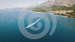 Speedboat carves a frothy trail in the calm Adriatic Sea. Above, a red parasail floats under a clear sky.