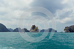 Speedboat sails through calm blue waters near large rock formations under a cloudy sky