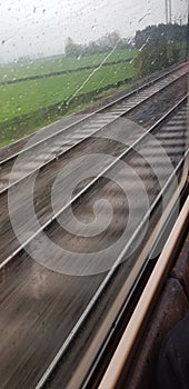 Speeding train tracks, trails of rain with meadows in the background