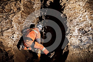 Speleologist descend by the rope in the deep vertical cave tunnel. Cave man hanging over abyss