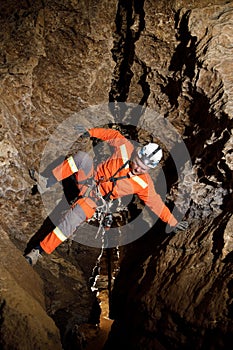 Speleologist descend by the rope in the deep vertical cave tunnel. Cave man hanging over abyss. View from the top og the tunnel.