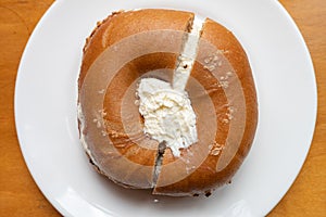 Spelt Bagel with Cream Cheese on a White Plate on a Wooden Table