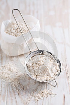 Spelt flour in sifter in flour bag on white wooden table