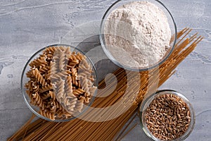 Spelt pasta, spelt grain and whole grain spelt flour in bowl and jar. Top view.