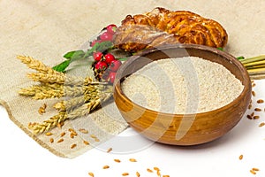 Spelt whole grain flour in ceramic bowl, wheat ears and homemade roll bun