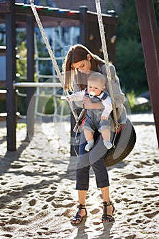 Spending a little time outdoors. Young mom on a park swing with a baby boy.