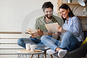 Spending nice time at home. Couple bonding to each other and smiling while reading book, tablet