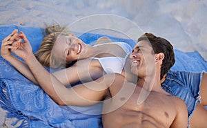 Spending quality time at the beach. A young couple lying together on a towel at the beach.