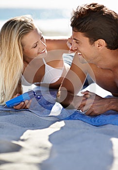 Spending quality time at the beach. A young couple lying together on a towel at the beach.