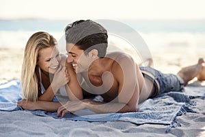 Spending quality time at the beach. A young couple lying together on a towel at the beach.