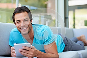 Spending some time online. Portrait of a handsome man lying on the sofa with his digital tablet.