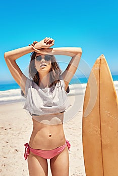 Spending time in the summer sun. Portrait of a sexy young woman standing on the beach with her surfboard.