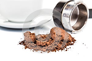 Spent or used coffee grounds with portafilter and a cup of freshly brewed coffee in the background photo