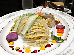 Sphagetti topped with cliced cucumber with pork steak on white plate