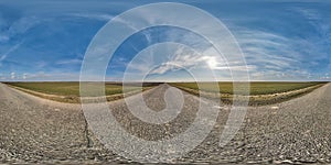 spherical 360 hdri panorama on old asphalt road with cracks with clouds and sun on blue sky in equirectangular seamless projection