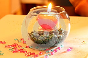 Spherical candle lit over small blue pebbles and small decorative blue and pink hemispheres