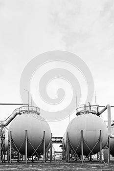 Spherical gas storage tank of chemical industry petrochemical plant under grey sky black and white BW vertical with