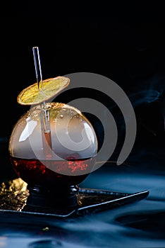 Spherical glass with smoke and alcohol. Caramelized Lemon Slices. Smoke on a black background.