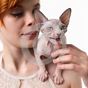 Sphynx Hairless kitten meowing, sitting on shoulder of redhead young woman. Close-up view