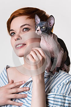 Sphynx kitten sitting on shoulder of happy redhead young woman. Selective focus on cat