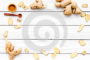 Spice and condiment. Ground ginger in small bowl near ginger root on white wooden background top view copy space