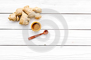 Spice and condiment. Ground ginger in small bowl near ginger root on white wooden background top view copy space