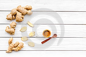 Spice and condiment. Ground ginger in small bowl near ginger root on white wooden background top view copy space