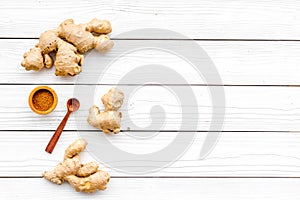 Spice and condiment. Ground ginger in small bowl near ginger root on white wooden background top view copy space