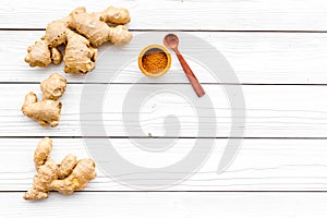 Spice and condiment. Ground ginger in small bowl near ginger root on white wooden background top view copy space