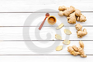 Spice and condiment. Ground ginger in small bowl near ginger root on white wooden background top view copy space