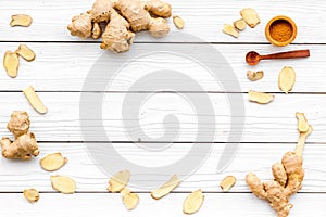 Spice and condiment. Ground ginger in small bowl near ginger root on white wooden background top view copy space