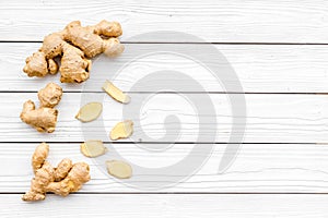 Spice and condiment. Ground ginger in small bowl near ginger root on white wooden background top view copy space