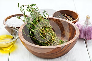 Spice ingredients: thyme, salt, pepper, chili, garlic, olive oil in bowls on white rustic wooden table
