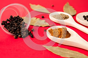 Spices: black pepper, ground red pepper and ground coriander on wooden spoons and Bay leaf on red background