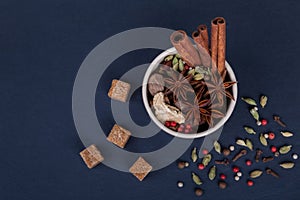 Spices cinnamon sticks, cardamom pods, star anise, sugar, nutmeg, coriander and pepper seeds in brown ceramic cup on a black slate