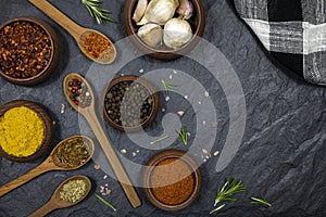 Spices and condiments in wooden utensils on black stone background. Free space for text