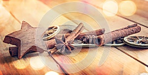 Spices with dried orange and cinnamon on wood background with blurred lights, christmas decor