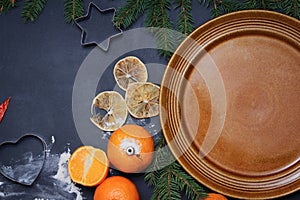 Spices flour orange pine tree branch and empty plate on a black board winter christmas background